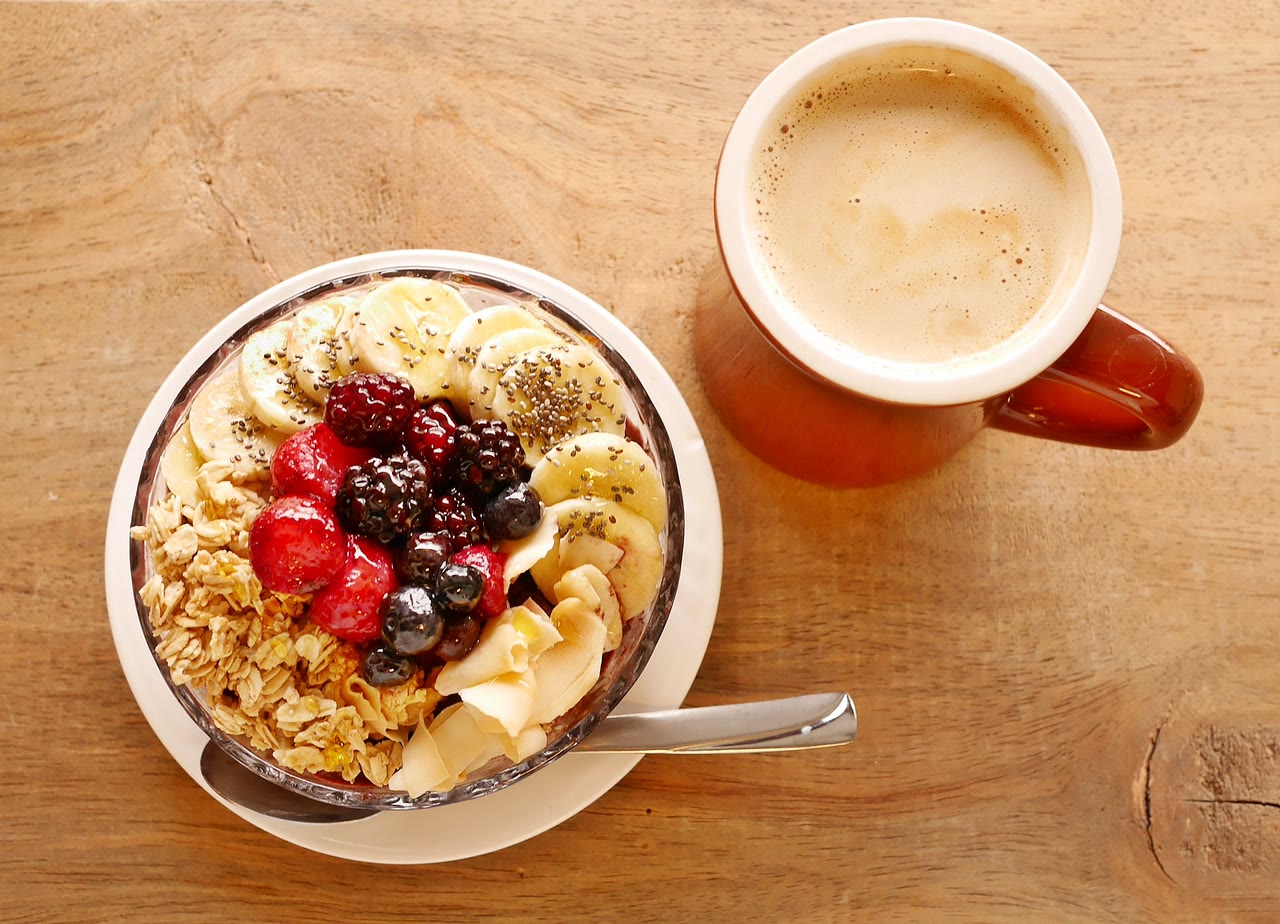 Granola bowl with banana, strawberries, blackberries, blueberries and coconut, next to a cup of coffee